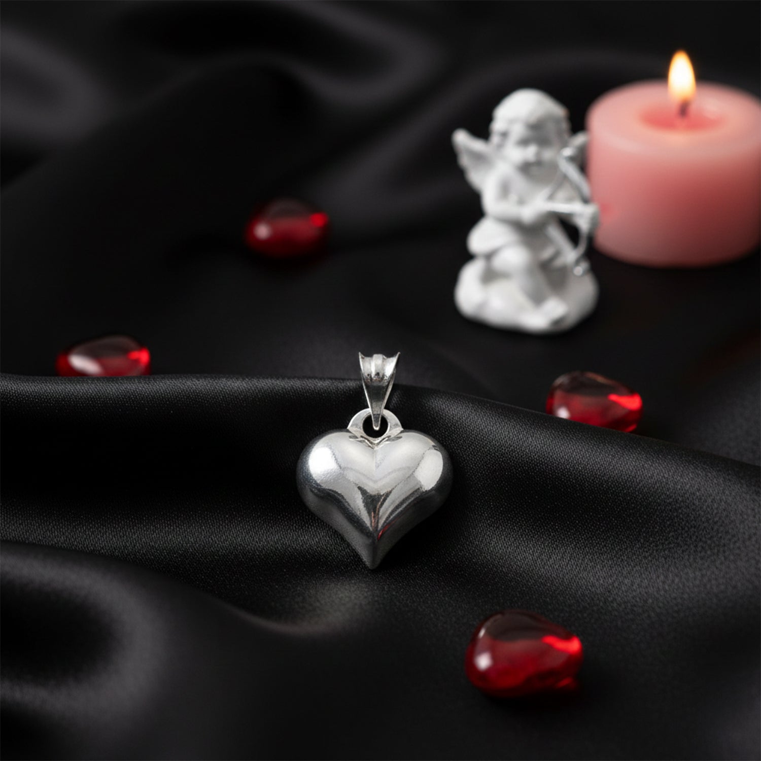 Silver heart-shaped pendant on black fabric with red gemstones and a small angel figurine.