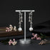 Silver earrings on a stand with flowers on a dark background