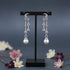 Pair of silver earrings with pink gemstones and pearl drops on a black stand with flowers in the background.