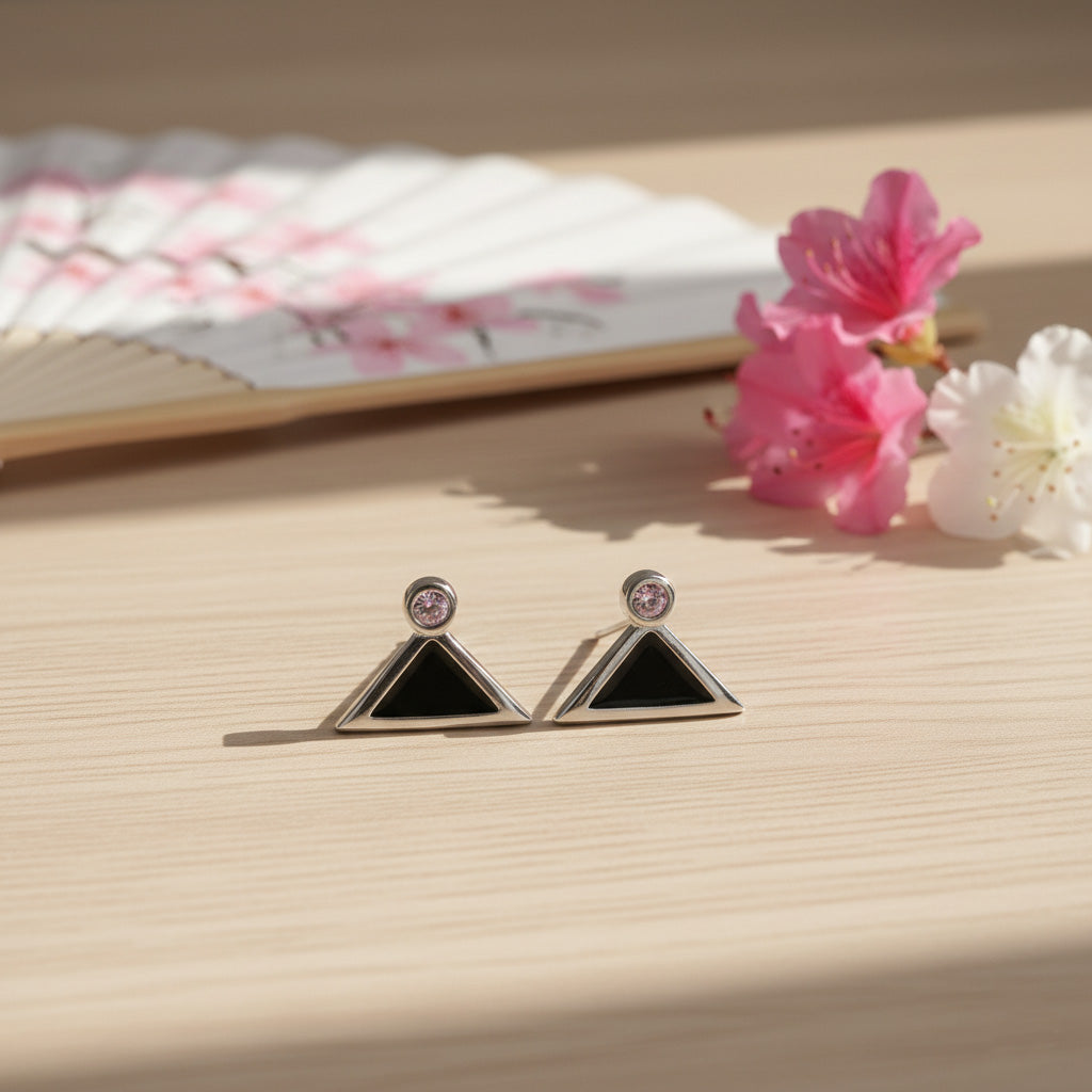 Triangle-shaped earrings with black centers and silver borders on a wooden surface with flowers.