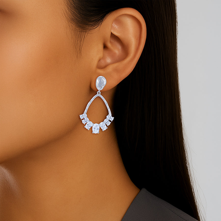 Close-up of a woman wearing a silver earring with clear gemstones on a neutral background