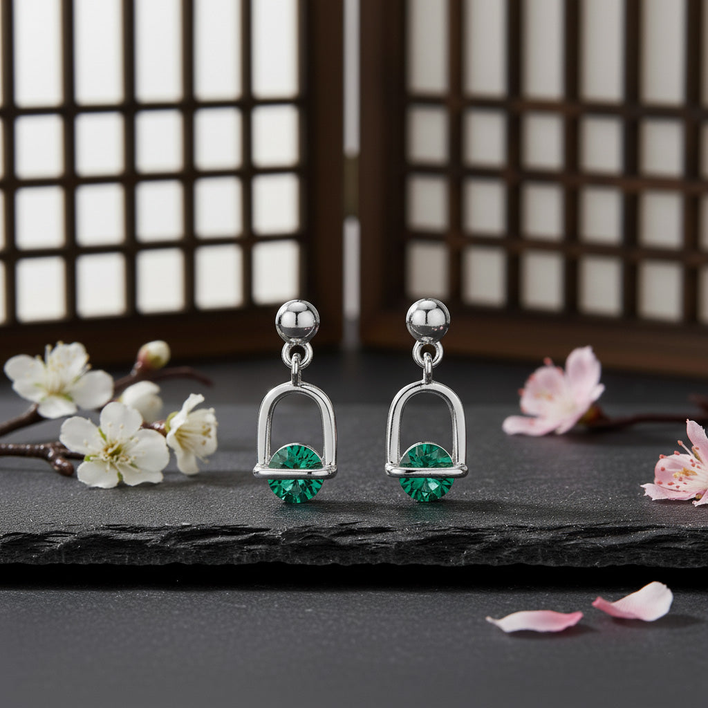 Silver earrings with green gemstones on a dark surface with flowers