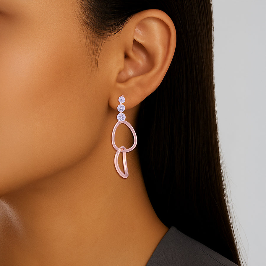 Close-up of an ear wearing a pink earring with clear stones on a neutral background