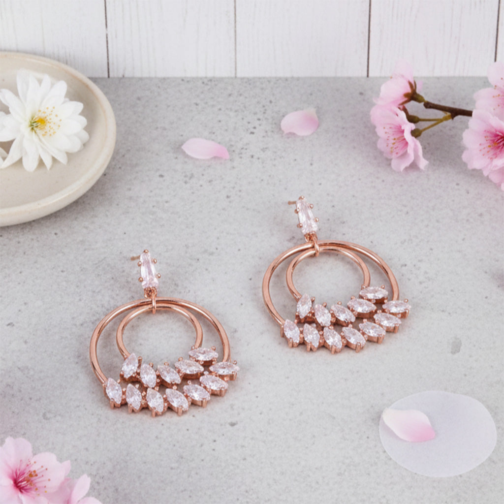 Rose gold earrings with clear stones on a light surface with flowers