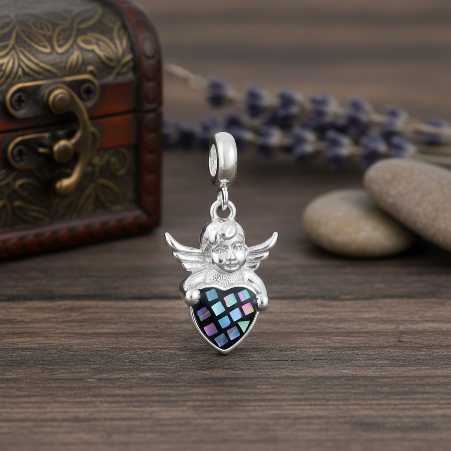 Silver angel pendant with a colorful heart on a wooden surface with decorative elements.