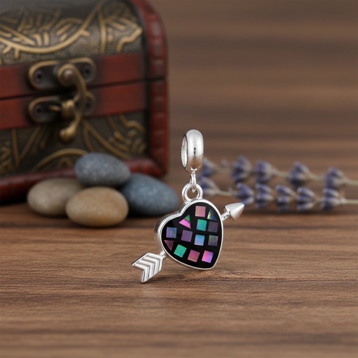 Silver charm with heart and arrow design on a wooden surface with decorative background