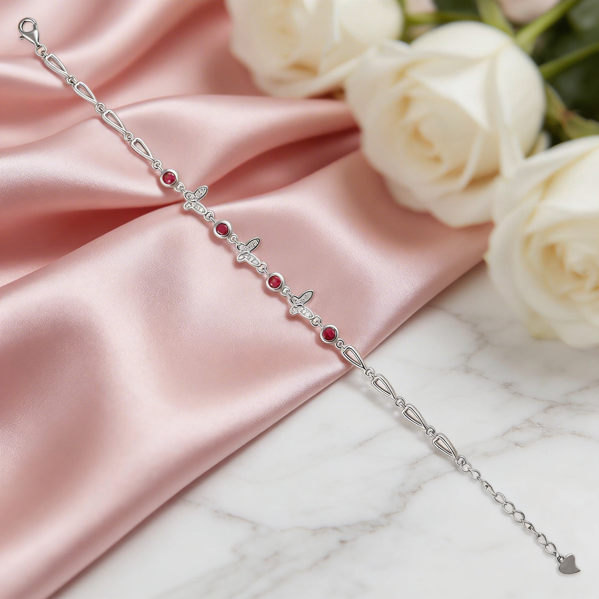Silver bracelet with red stones on a pink satin cloth with white roses in the background