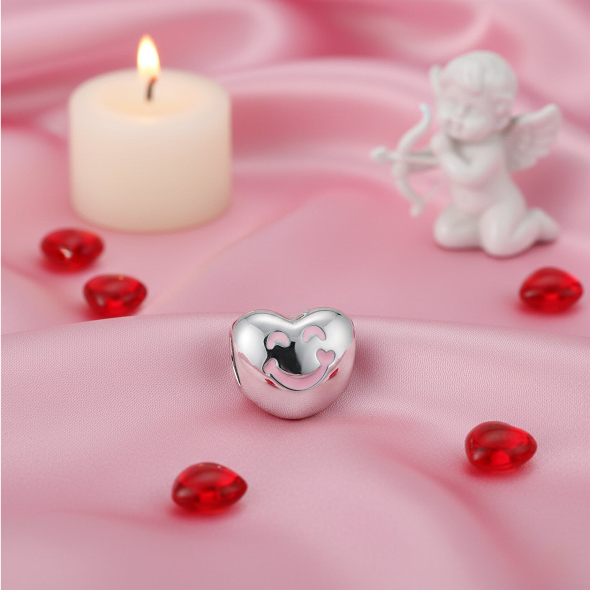 Silver heart-shaped charm on a pink fabric background with red gemstones and a candle.