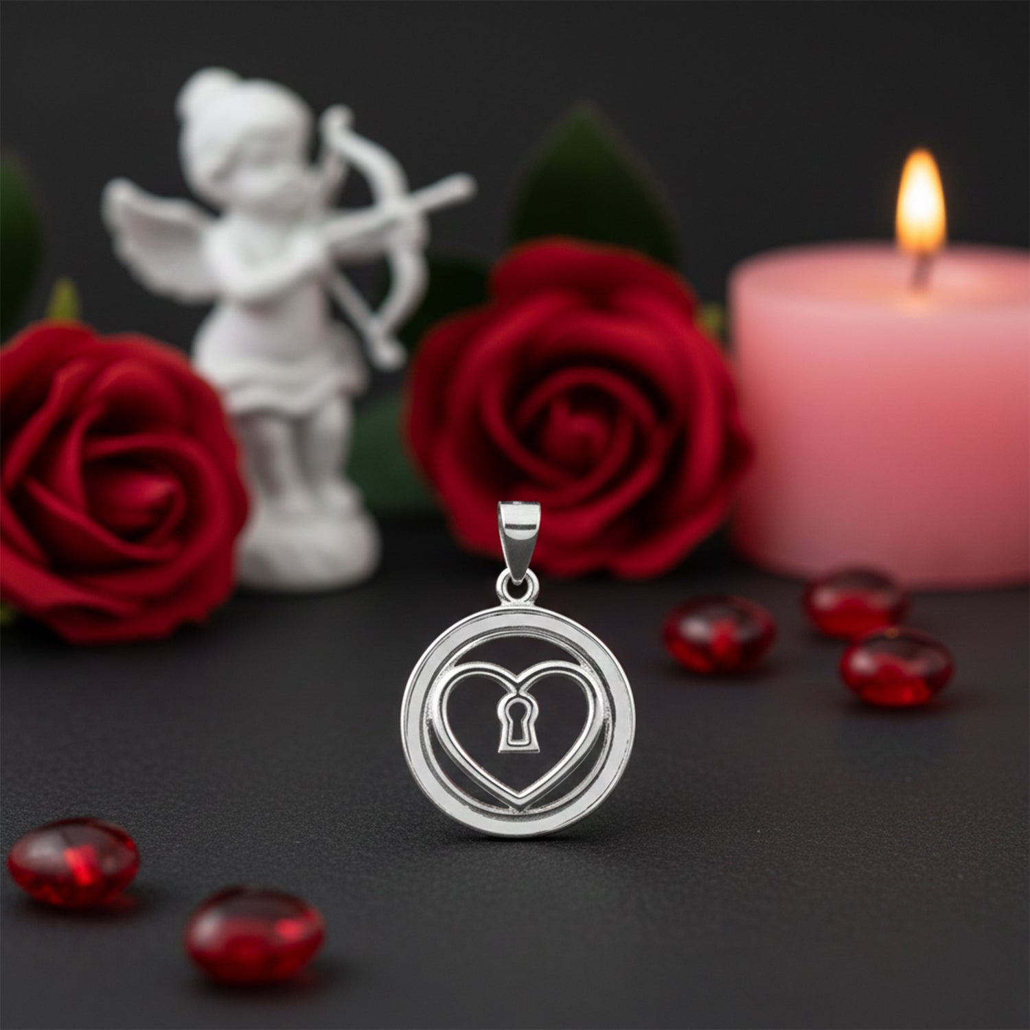Silver heart-shaped pendant with keyhole design on a dark surface with red roses, a candle, and a small statue.