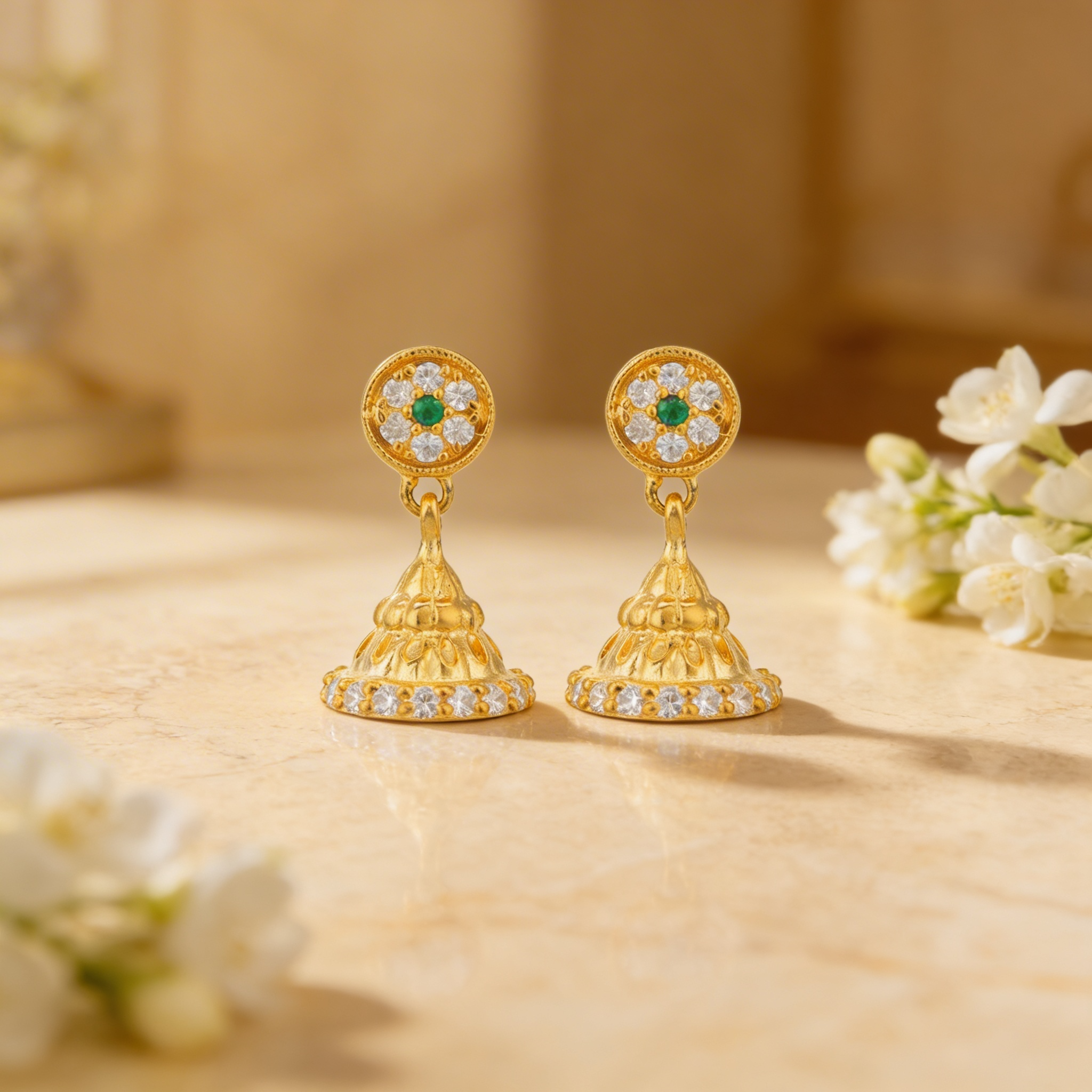 Gold earrings with green and white stones on a beige surface with flowers.