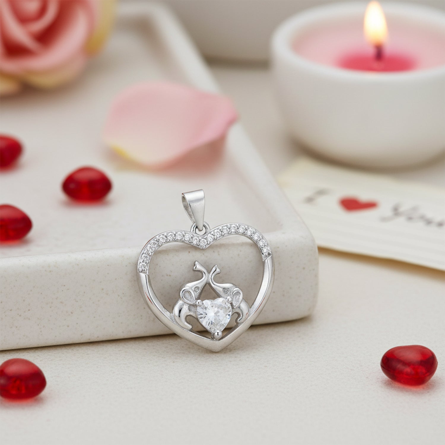 Silver heart-shaped pendant with a diamond on a romantic setting with candles and flowers.