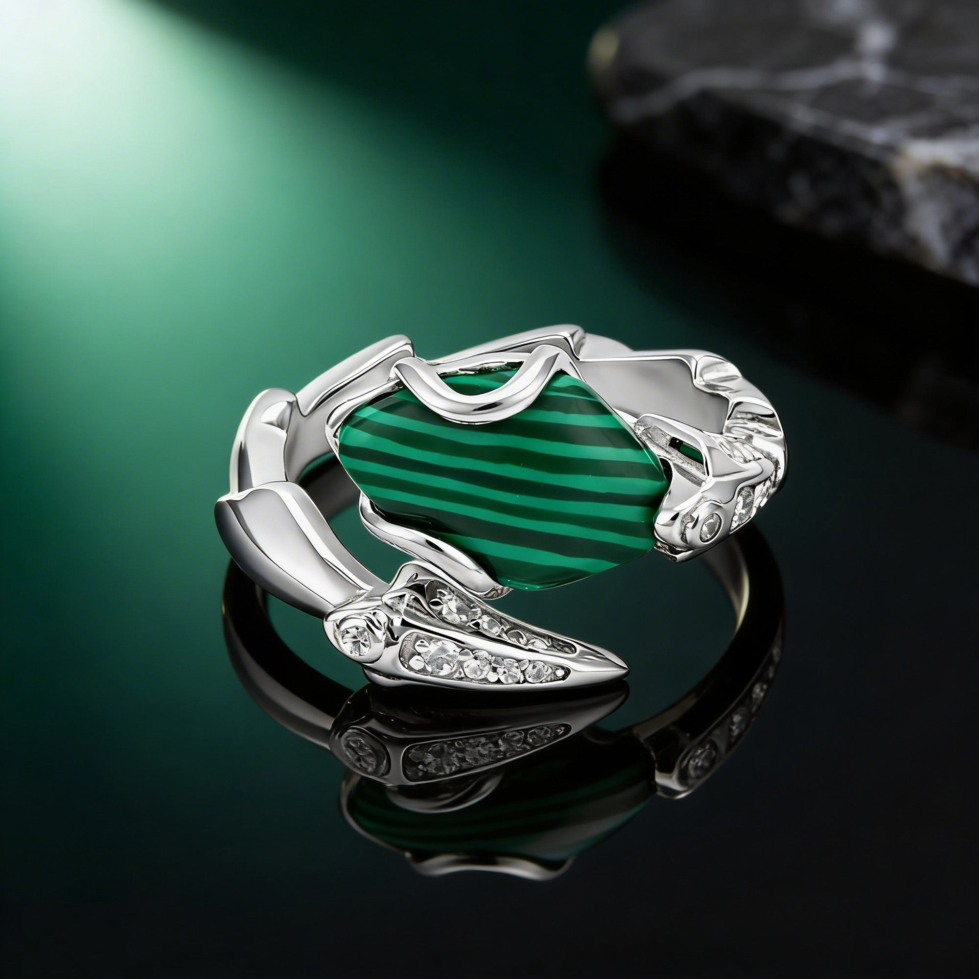 Silver ring with green gemstone on a reflective surface