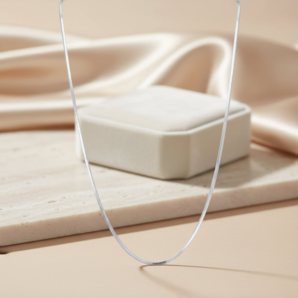Silver necklace on a beige surface with a jewelry box in the background