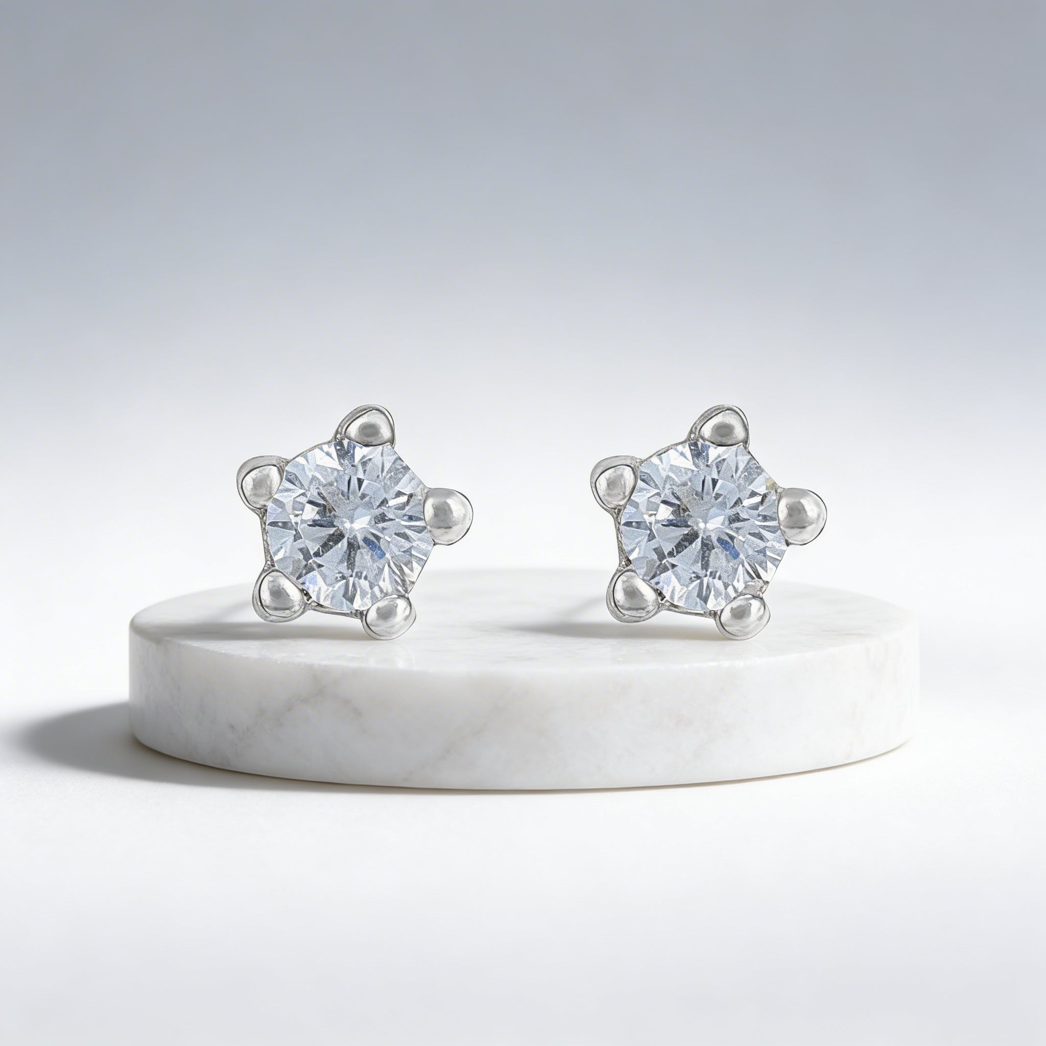 Pair of silver stud earrings with clear gemstones on a white platform.