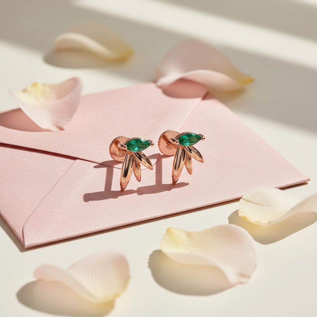 Rose gold earrings with green gemstones on a pink card with flower petals