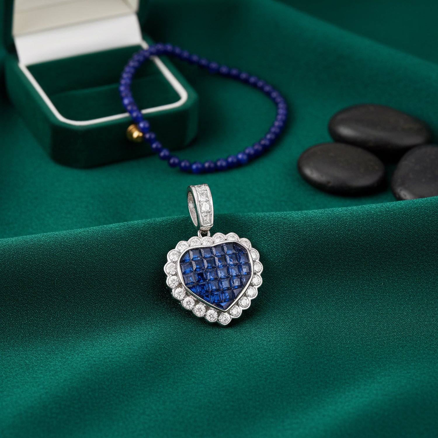 Heart-shaped silver pendant with blue gemstones on a green fabric background