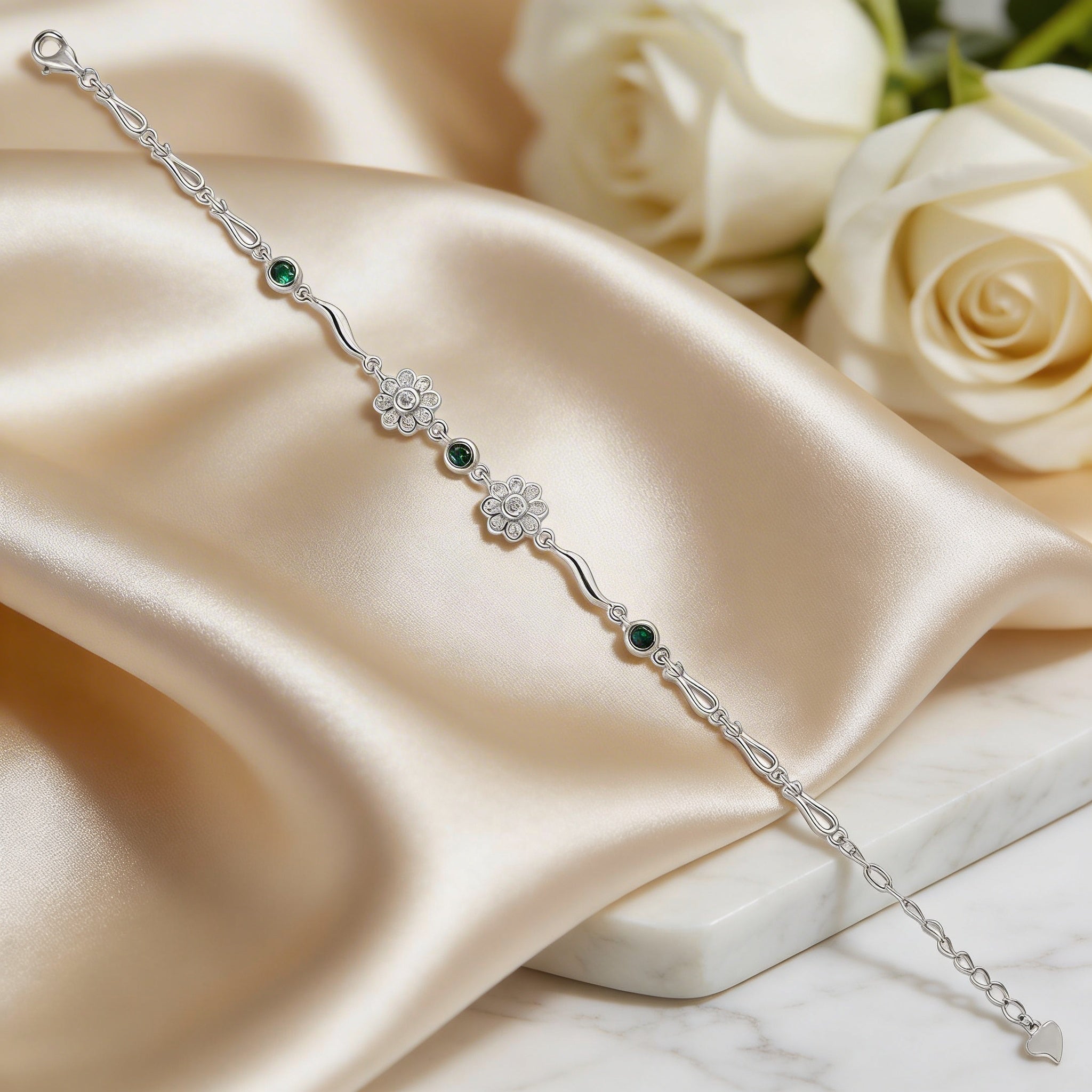 Silver bracelet with green gemstones on a satin surface with white roses