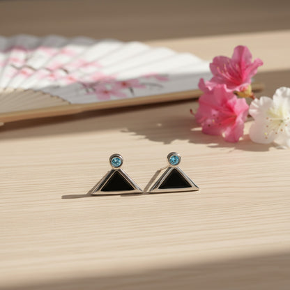 Pair of triangle-shaped earrings with gemstones on a wooden surface with flowers.