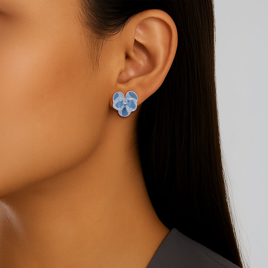 Close-up of a person wearing blue floral earrings with a neutral background