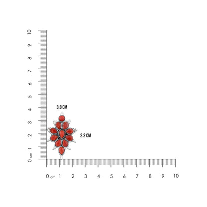 Floral brooch with red stones next to a ruler on a white background