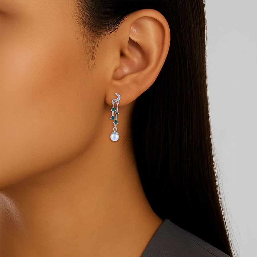 Close-up of a person wearing a dangling earring with green gemstones on a neutral background