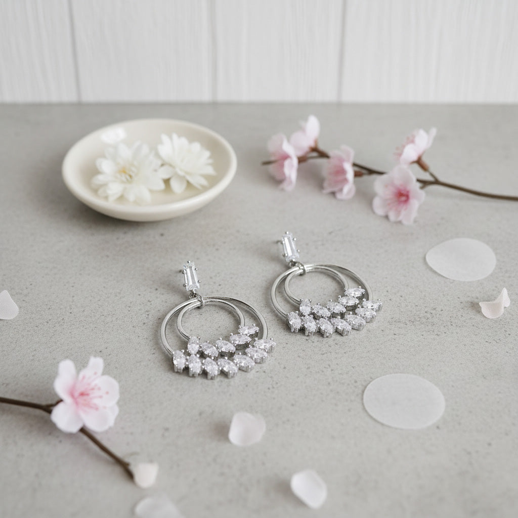 Silver hoop earrings with floral designs on a light surface with flowers and petals.