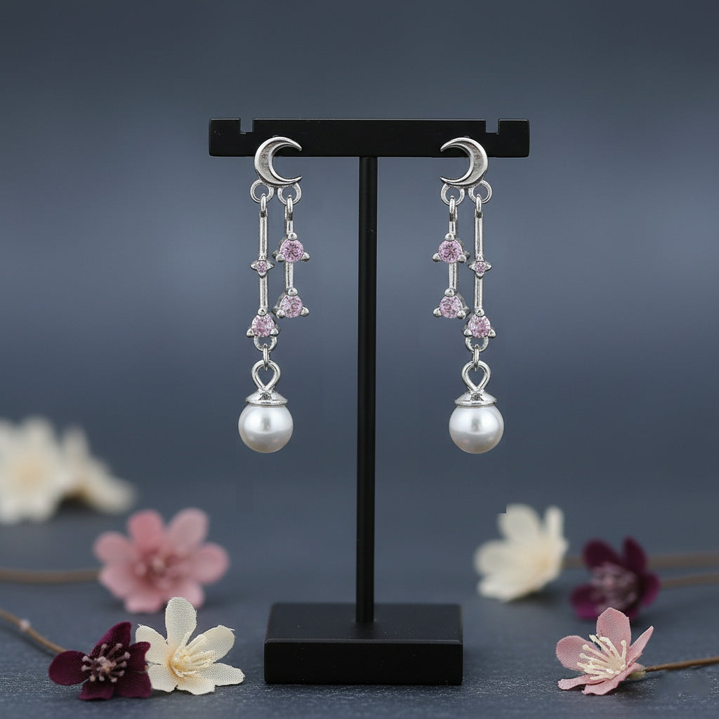 Pair of silver earrings with pink gemstones and pearl drops on a black stand with flowers in the background.