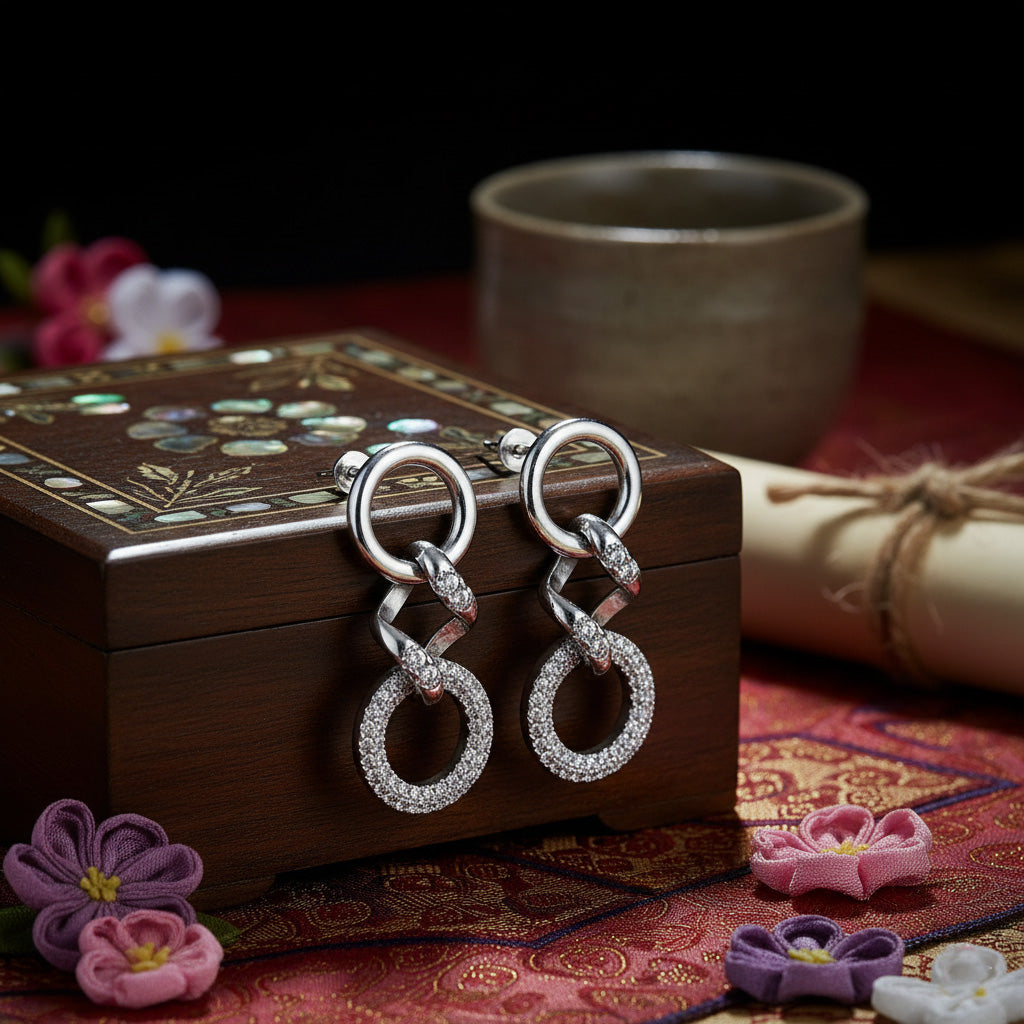 Silver earrings on a decorative box with flowers and a cup in the background