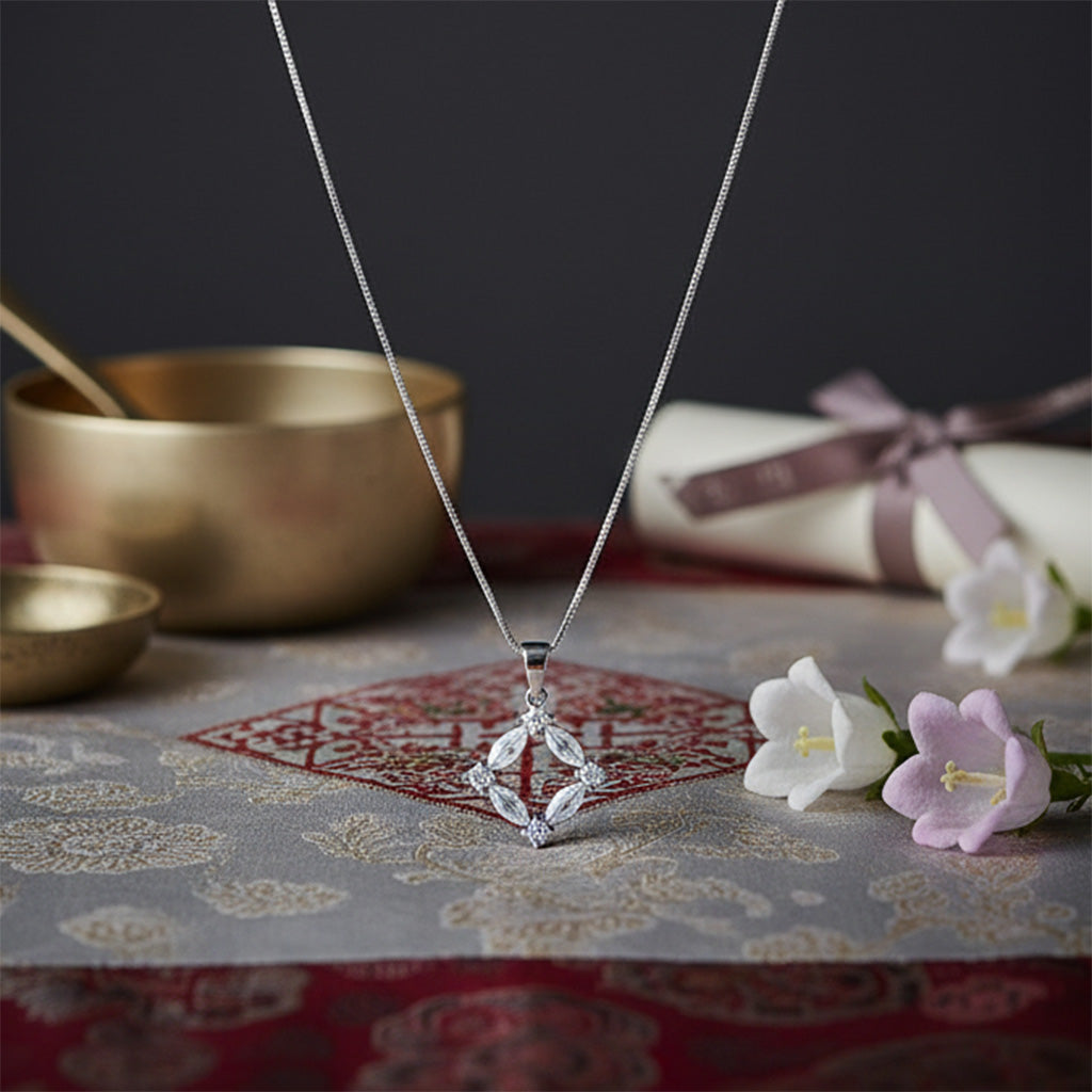 Silver necklace with a diamond pendant on a patterned surface with flowers and bowls.
