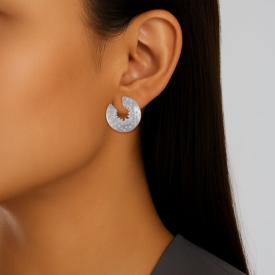 Close-up of an ear wearing a silver earring with a dark background