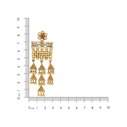 Gold earrings with a red gemstone next to a ruler for scale on a white background