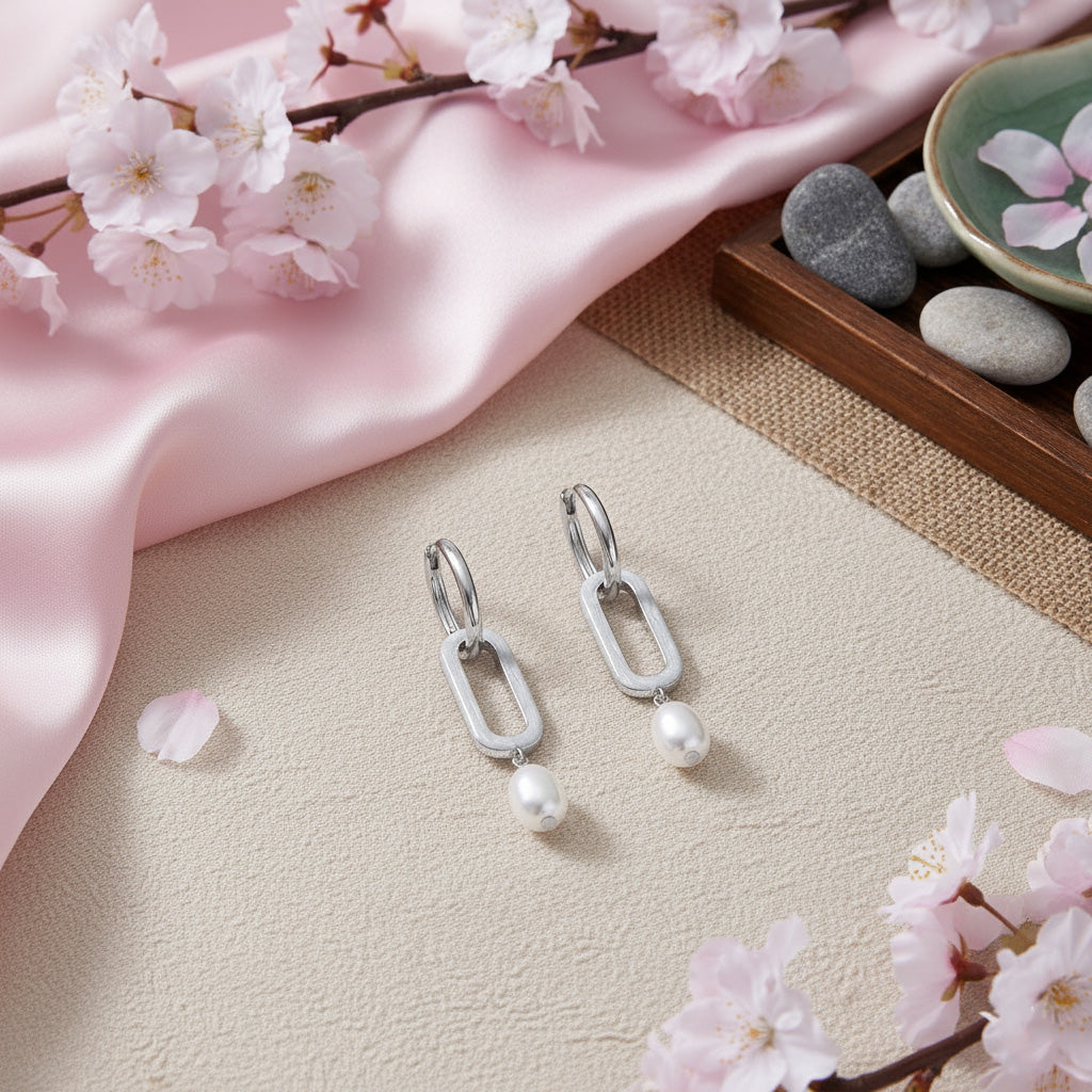 Silver earrings with pearls on a light surface with cherry blossom branches and pink fabric.