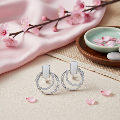 Silver earrings on a beige surface with cherry blossoms and pink petals.