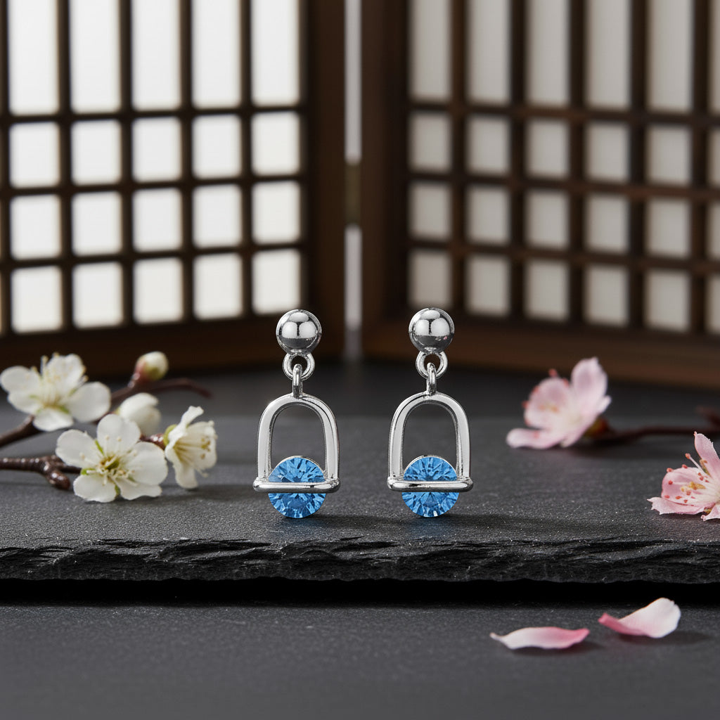Silver earrings with blue gemstones on a dark surface with flowers