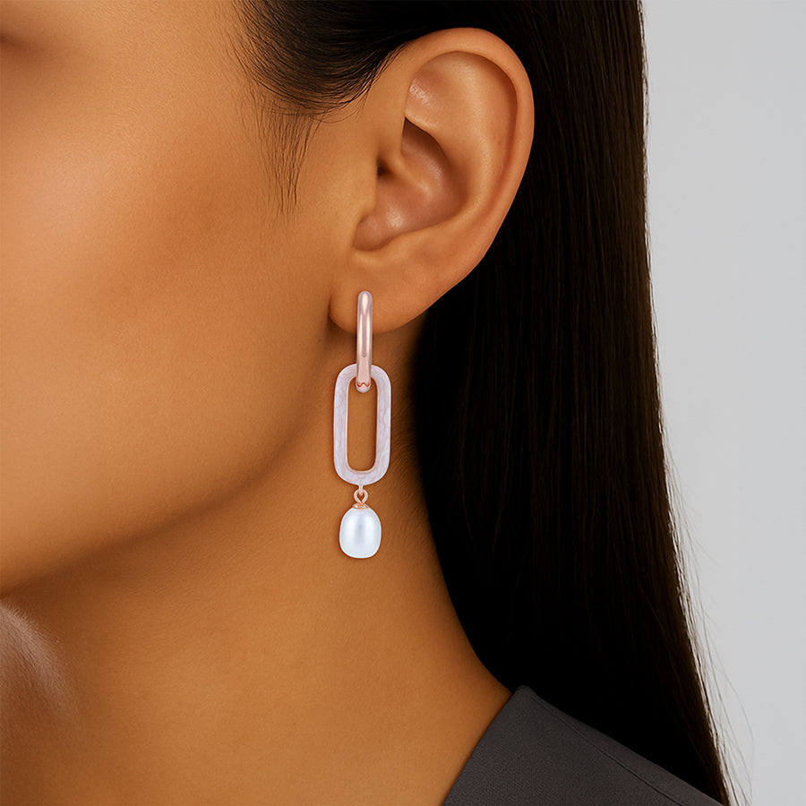 Close-up of an ear wearing a unique earring with a pearl drop on a neutral background