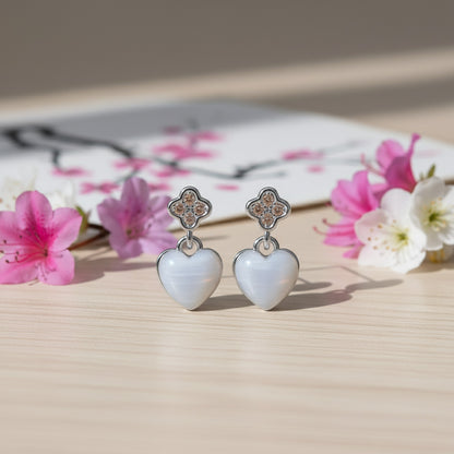 Heart-shaped earrings with floral design on a wooden surface with flowers in the background