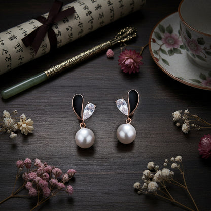 Pearl earrings on a dark surface with flowers and a tea cup in the background