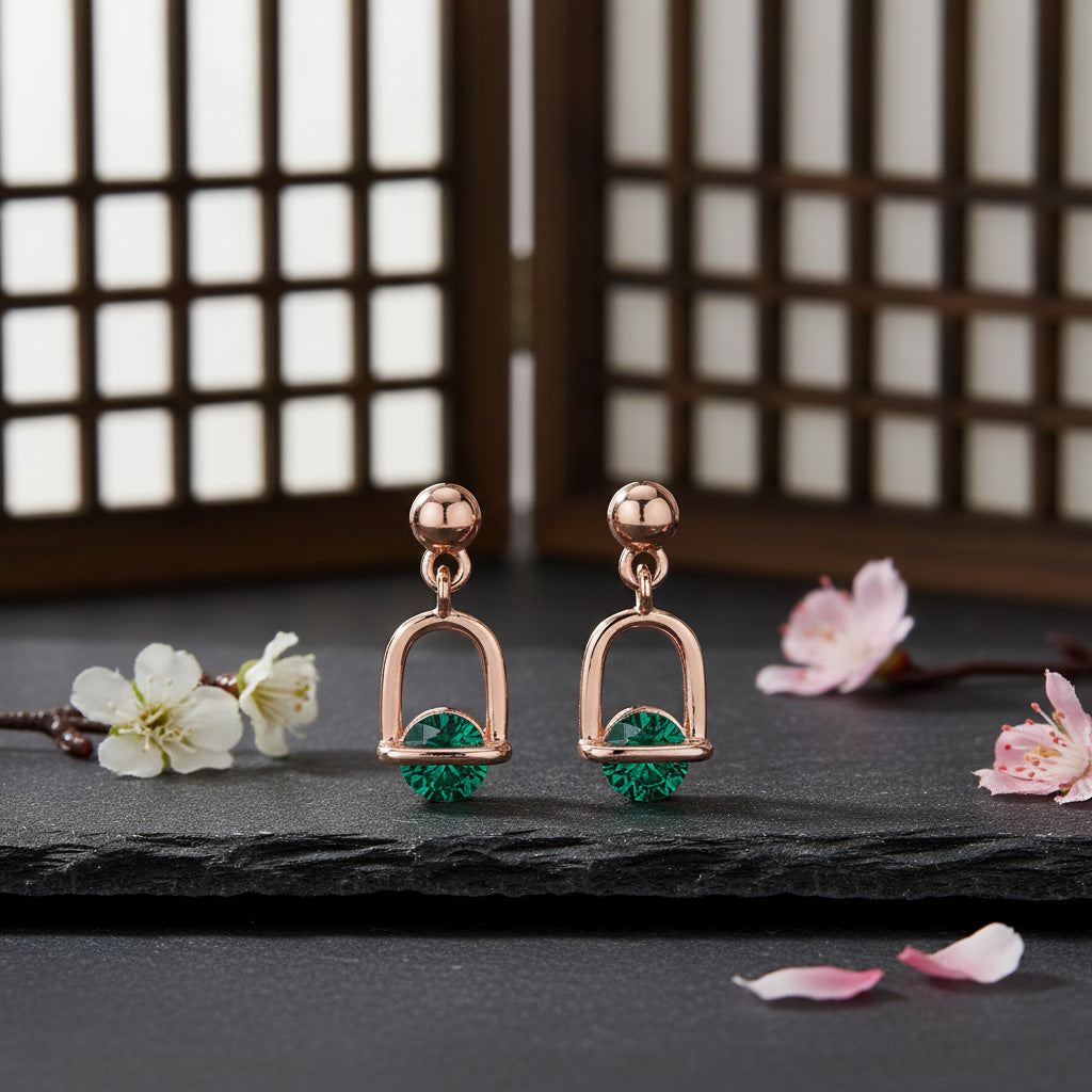 Rose gold earrings with green gemstones on a dark surface with floral decorations.