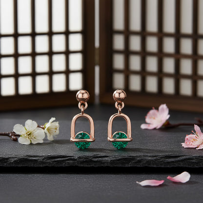 Rose gold earrings with green gemstones on a dark surface with floral decorations.