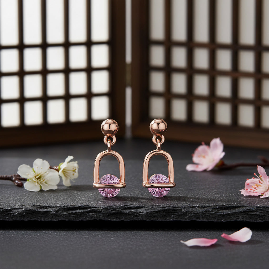 Rose gold earrings with pink gemstones on a dark surface with cherry blossom flowers.