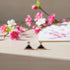 Triangle-shaped earrings with gemstones on a wooden surface with flowers in the background