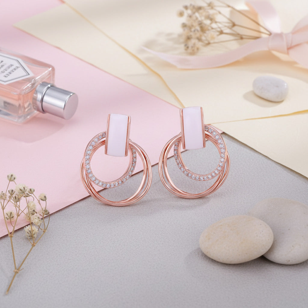 Rose gold hoop earrings with white stones on a soft pastel background