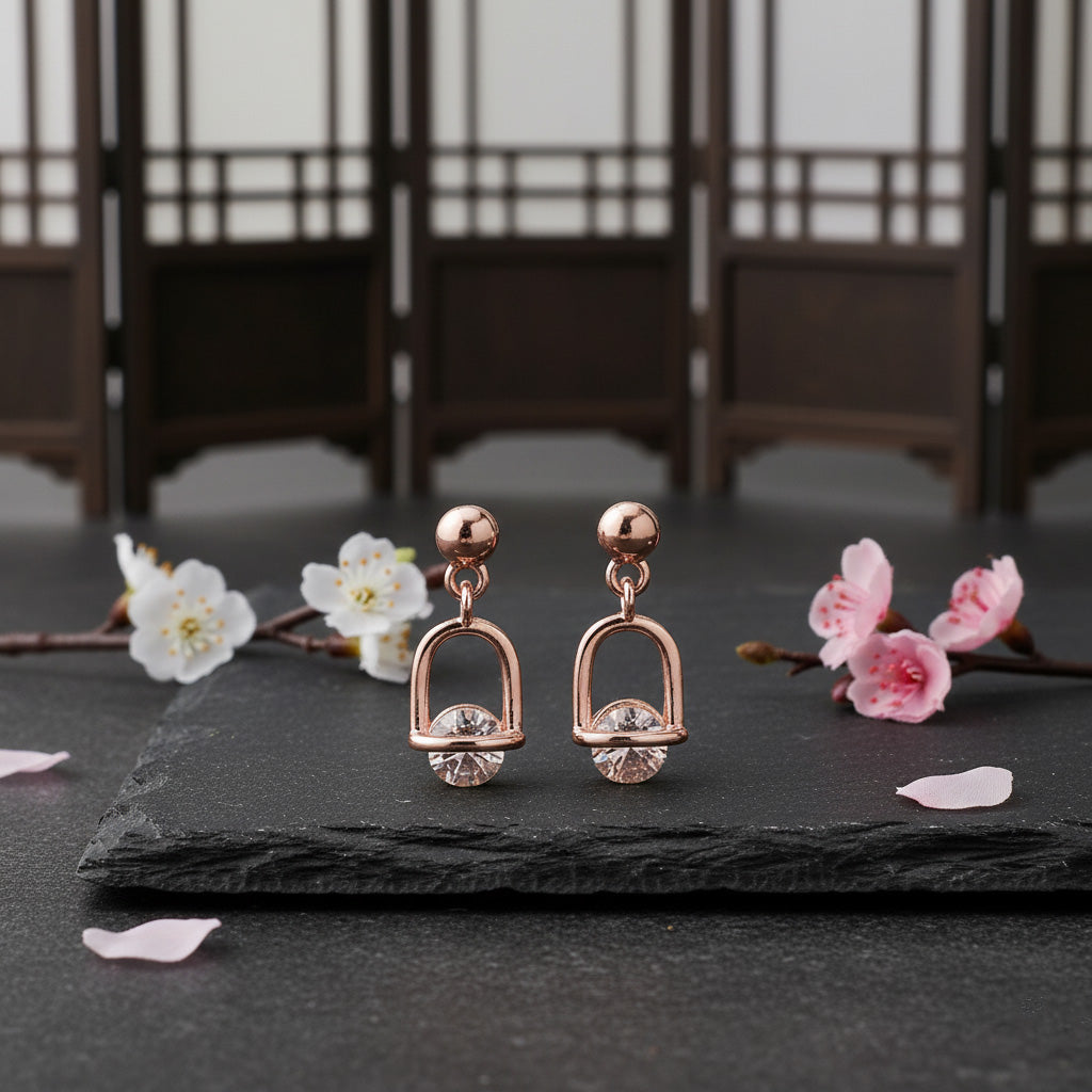 Rose gold earrings with crystals on a black slate surface with cherry blossoms.