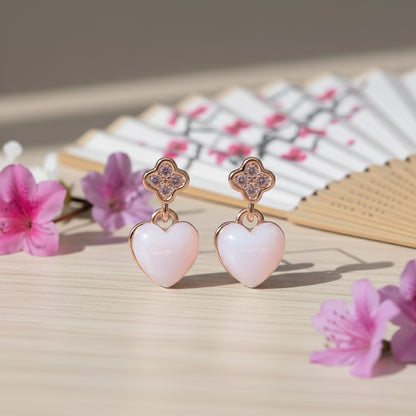 Heart-shaped earrings with clover-like tops on a wooden surface with pink flowers.