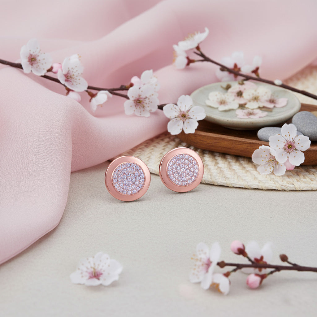 Rose gold earrings with diamond accents on a soft pink fabric background with cherry blossoms.