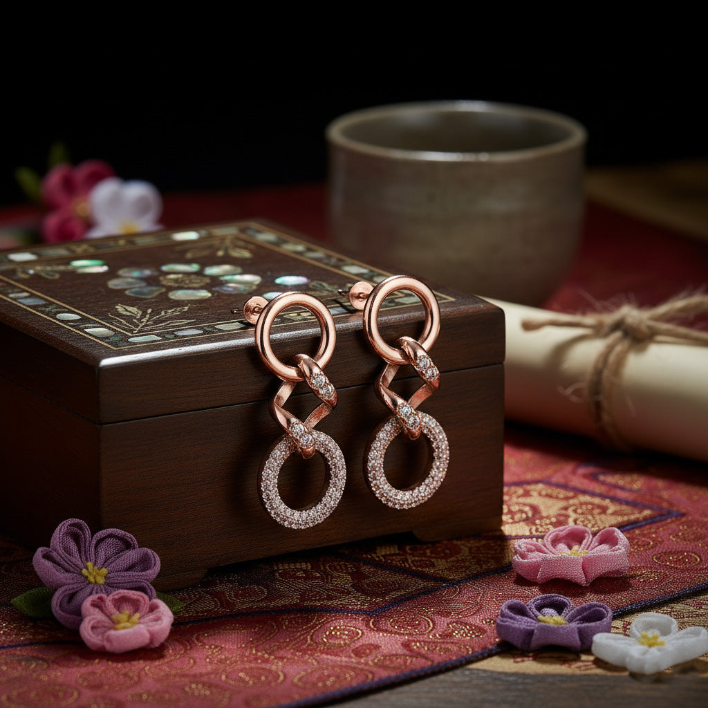 Rose gold earrings with diamond accents on a decorative box with flowers and a cup in the background.