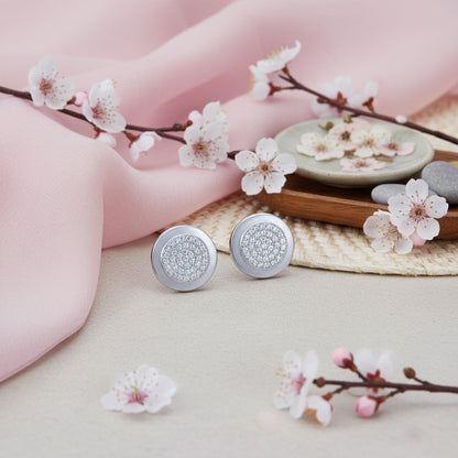 Silver earrings with floral design on a soft pink fabric background with cherry blossom branches.
