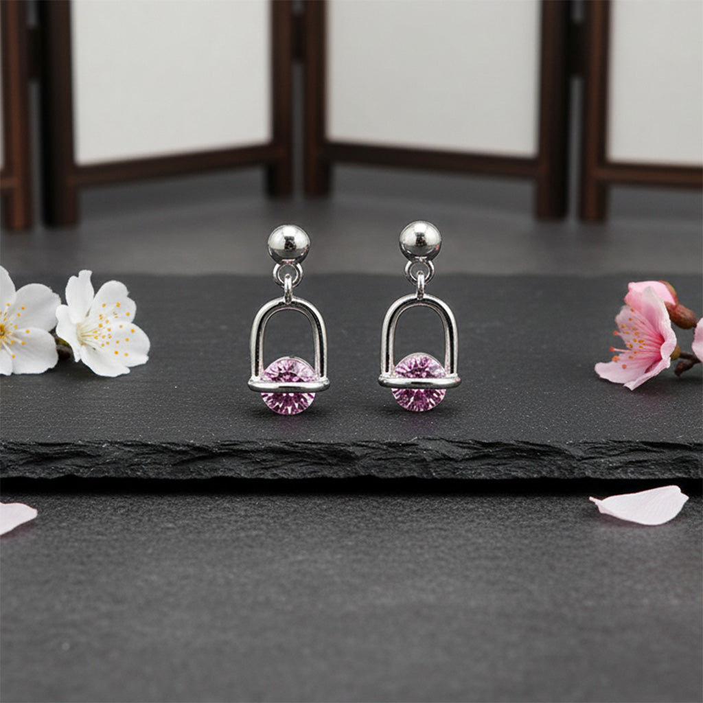 Silver earrings with pink gemstones on a dark surface with flowers.
