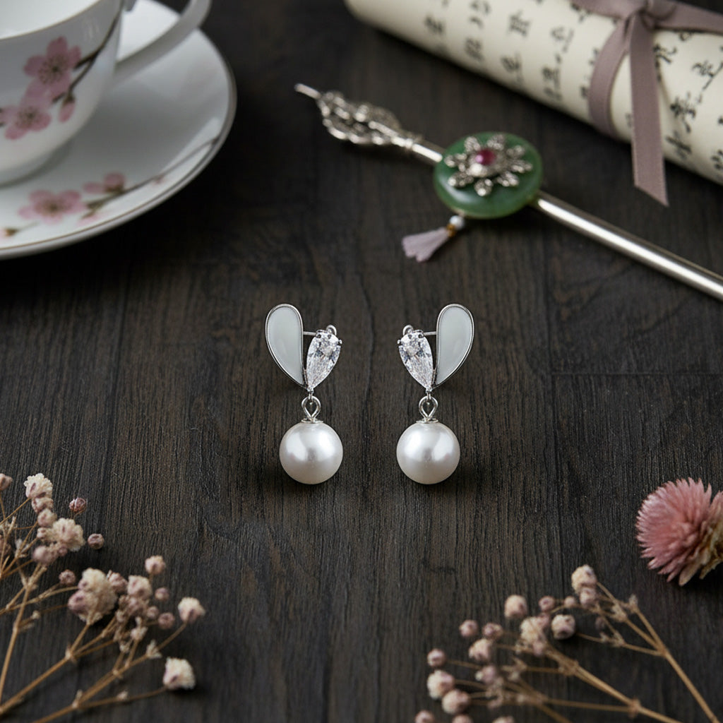 Pearl earrings on a dark wooden surface with a teacup and decorative items.