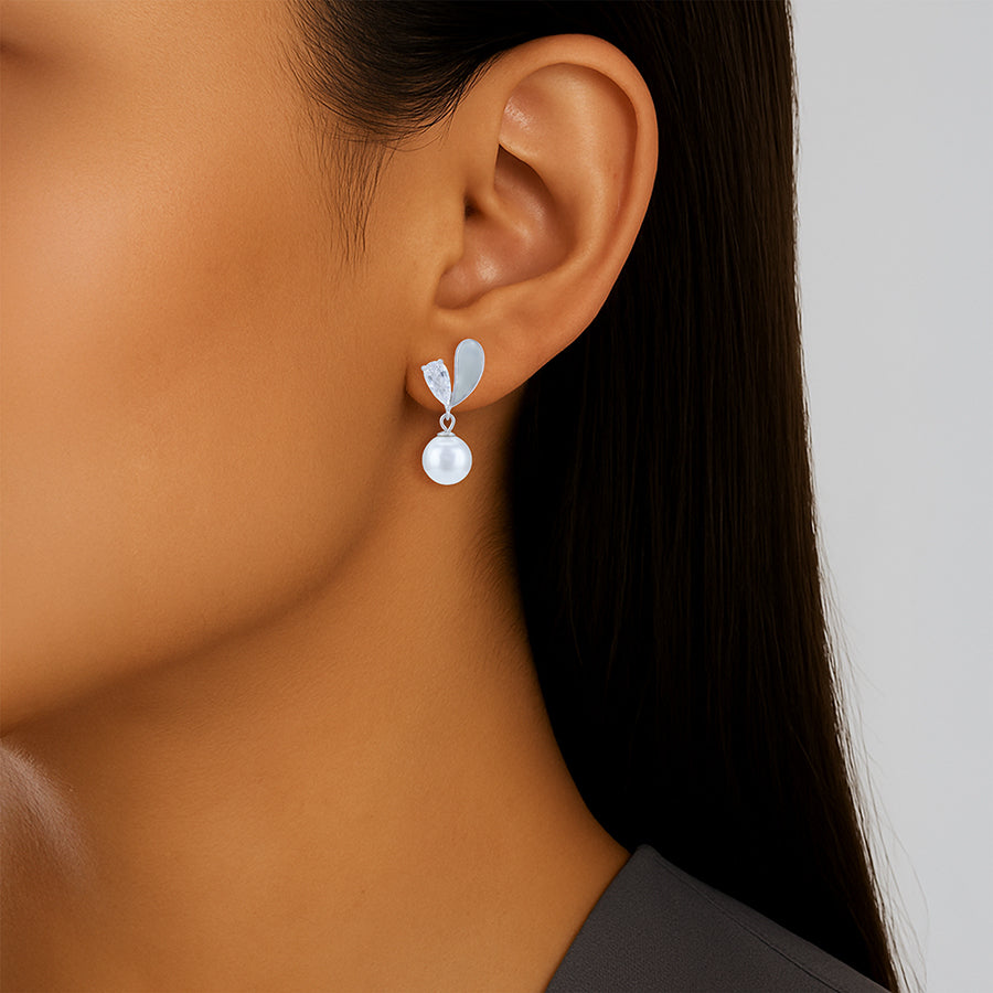 Close-up of a woman wearing a silver earring with a pearl-like center on a neutral background